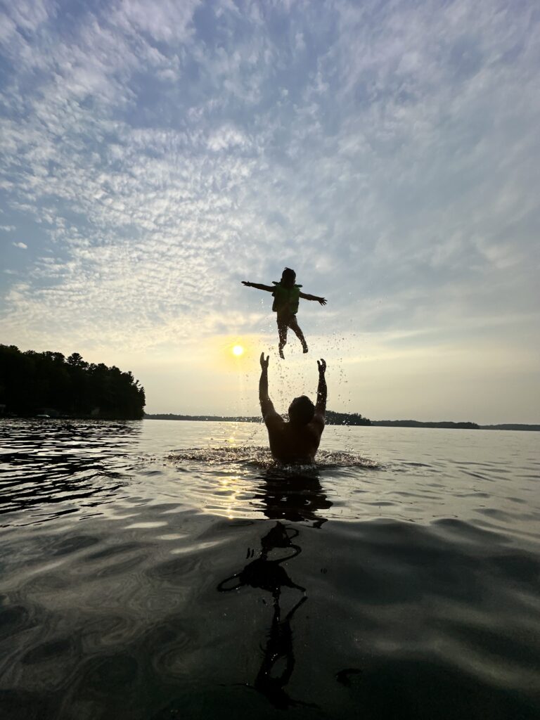 image of a grandmother in an Ontario lake, tossing a child in a life jacket up above her